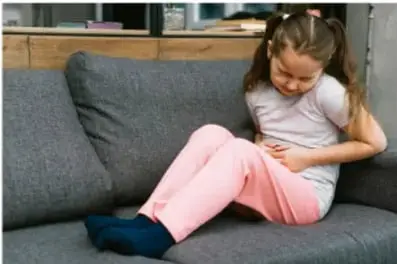 Niña sentada en un sillón tocándose el abdomen.