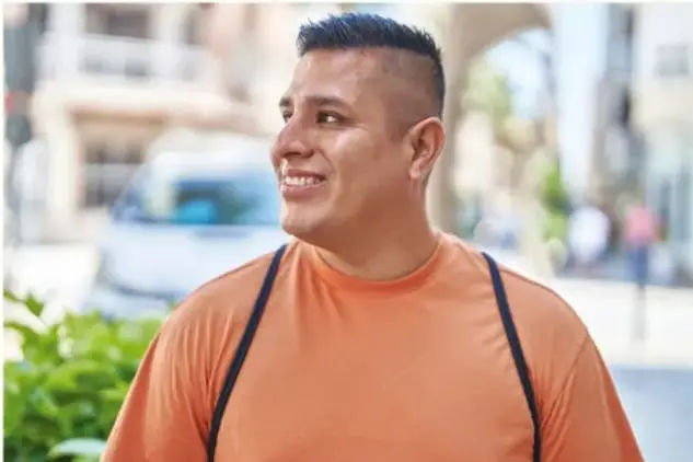 Fotografía de un joven sonriente con camiseta anaranjada, al aire libre, que ilustra la persona de la rutina descrita.