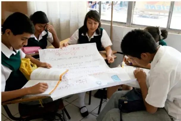 Fotografía de estudiantes de secundaria trabajando en equipo alrededor de una mesa, elaborando un cartel escrito a mano sobre prevención de la violencia.