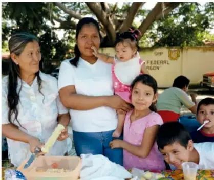 Escena 2: una chef conversa con un grupo de personas (mujeres, niñas y niños) que prueban su comida en un espacio comunitario.
