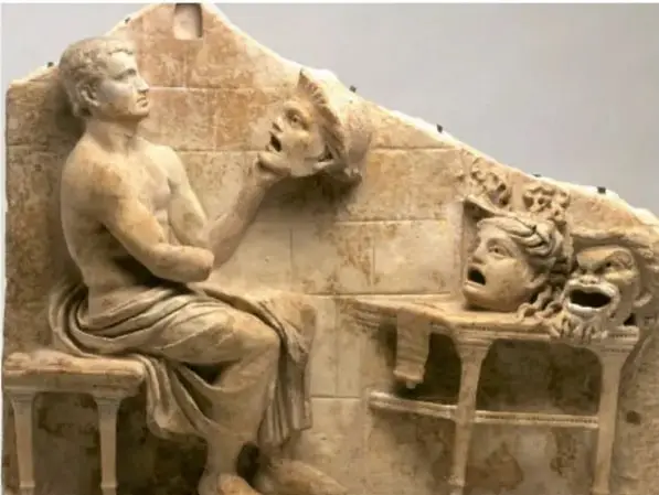 Relieve escultórico que muestra a un actor griego sentado sosteniendo dos máscaras teatrales, una trágica y una cómica.