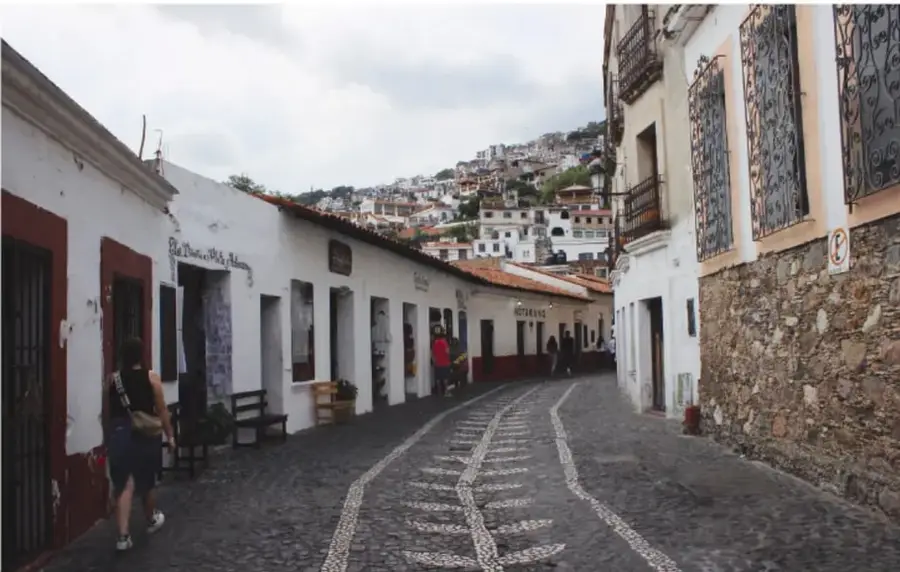 Fotografía de una calle empedrada y estrecha con casas de paredes blancas y tejados rojos, propia de un pueblo mágico o centro histórico, que muestra la herencia colonial de una localidad.