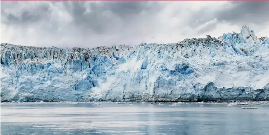 Fotografía de un glaciar azul con paredes de hielo y agua en primer plano.