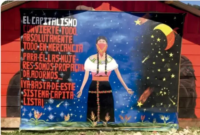 Mural con fondo azul estrellado y una figura femenina con vestimenta indígena; a la izquierda, un texto en letras rojas que dice: 'El capitalismo lo convierte todo absolutamente todo en mercancía para él las mujeres somos procreadoras, adornos y basta de este sistema capitalista'.