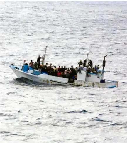 Fotografía de una embarcación pequeña y blanca, sin cubierta, sobrecargada de personas, navegando en aguas abiertas con oleaje moderado.