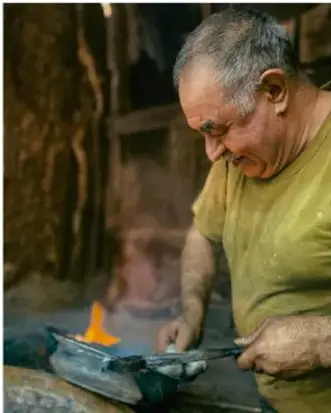 Fotografía de un artesano adulto trabajando con fuego y metal en un taller, ilustrando la práctica artesanal y la técnica tradicional.