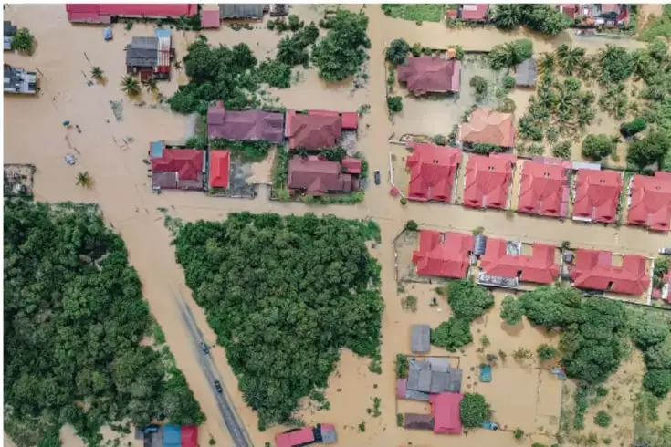 Fotografía aérea de una comunidad inundada: se observan viviendas con techos rojos, calles cubiertas por agua lodosa, árboles y áreas verdes parcialmente sumergidos, evidencia de precipitación extrema.