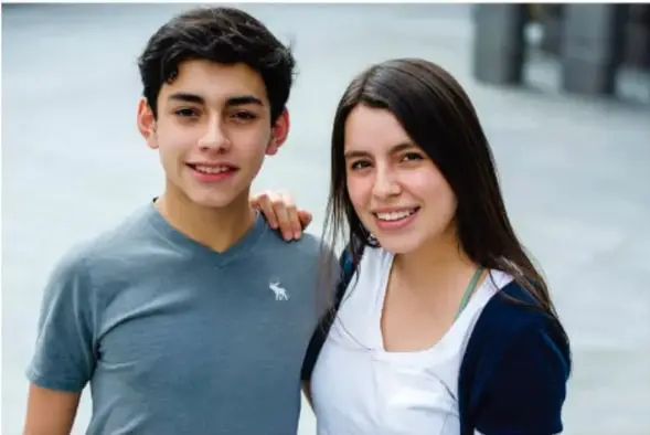 Retrato de dos adolescentes, un chico y una chica sonrientes, abrazados por el hombro al aire libre.
