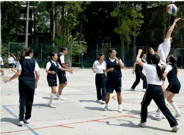Fotografía de un grupo de estudiantes jugando voleibol en una cancha al aire libre.