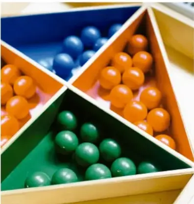 Caja triangular de madera con compartimentos que contienen bolas de colores azul, naranja y verde, usada como ejemplo de resultados posibles en un experimento aleatorio.
