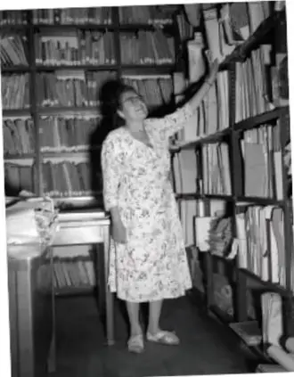 Fotografía en blanco y negro de la arqueóloga Eulalia Guzmán frente a estanterías de archivo con documentos.