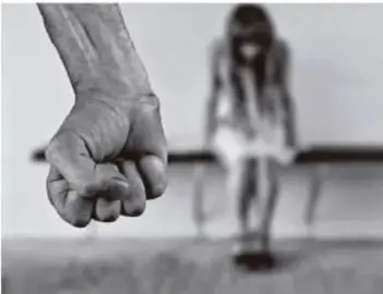 Fotografía en blanco y negro de un puño apretado en primer plano y, al fondo, una persona sentada con la cabeza agachada, ilustrando una situación de riesgo o vulnerabilidad social.
