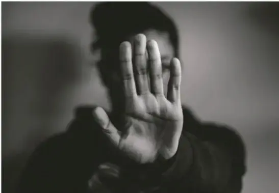 Fotografía en blanco y negro de una persona levantando la mano en gesto de detenerse, sugiriendo rechazo o protección frente a la violencia.