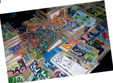Fotografía de varias cajas de cartón decoradas con dibujos coloridos y letras, apiladas, que parecen contener materiales o juegos elaborados por los estudiantes.