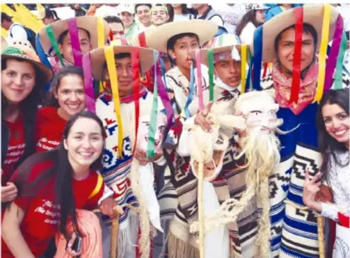 Fotografía de un grupo de jóvenes y adultos con sombreros de palma y cintas de colores, participando en una festividad comunitaria al aire libre, posando sonrientes.