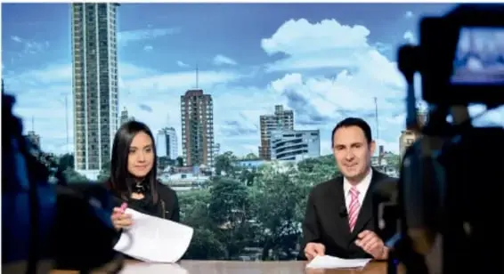 Dos presentadores de noticias en un estudio de televisión, con una ciudad de fondo.
