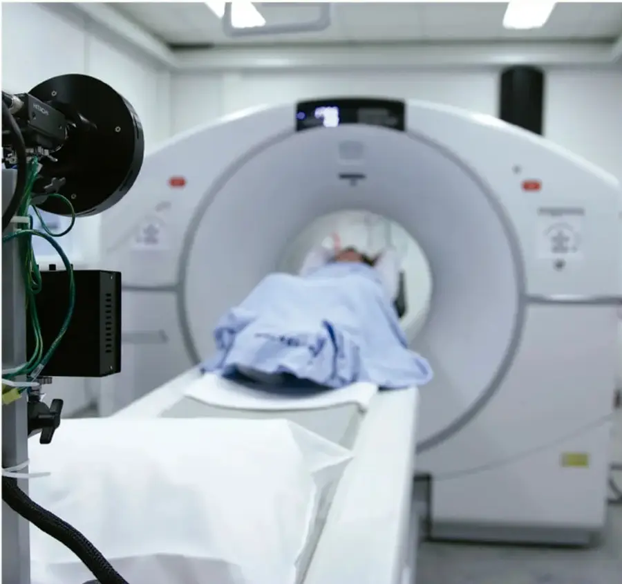 Fotografía de una persona recostada ingresando a un tomógrafo o equipo de diagnóstico por imagen médica (tomografía o resonancia magnética), en una sala hospitalaria.
