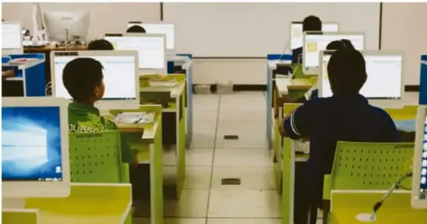 Fotografía de un aula o laboratorio de cómputo escolar con estudiantes sentados frente a computadoras, ilustrando el uso de internet en el entorno educativo.