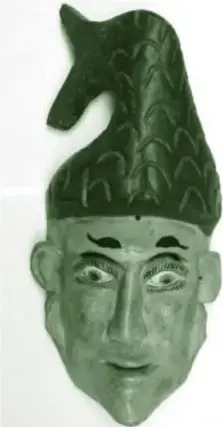 Máscara de madera pintada de verde con figura de animal en la parte superior (parece un venado o conejo) y rostro humano con cejas marcadas.