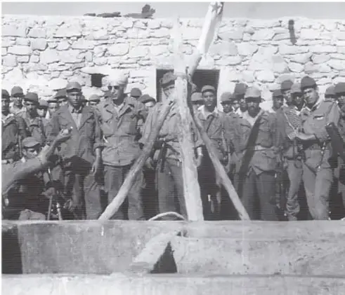 Fotografía en blanco y negro de un grupo de soldados o milicianos armados frente a un muro de piedra, posiblemente durante la guerra de Argelia.