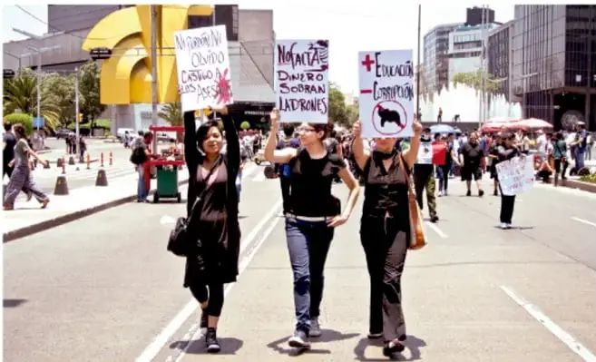 Fotografía de una marcha ciudadana en una avenida; tres mujeres al frente sostienen carteles con consignas sobre derechos, educación y libertad.