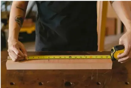 Persona midiendo una tabla de madera con un flexómetro.