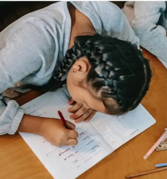 Niña escribiendo en un cuaderno sobre un escritorio, con lápices de colores.