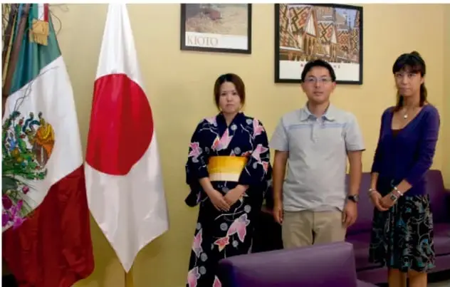Tres personas posando frente a las banderas de México y Japón; una de ellas viste un kimono con obi amarillo; al fondo hay un póster con la palabra "KIOTO", símbolo del aporte cultural japonés en México.