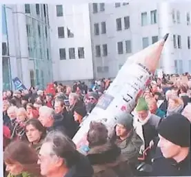 Fotografía de una concentración pública con personas reunidas y un cartel en primer plano.