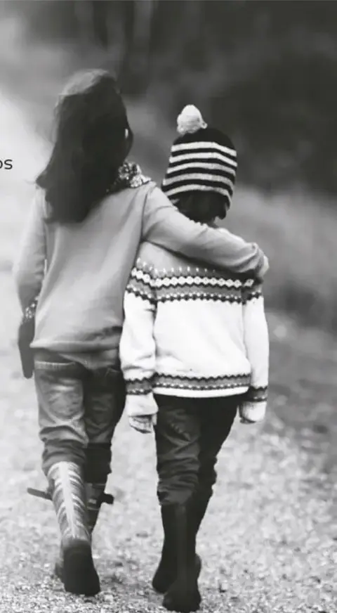 Fotografía en blanco y negro de una mujer que abraza a un niño con gorro de rayas mientras caminan por un camino rural; simboliza el éxodo migrante.