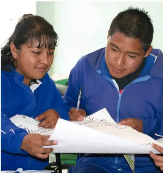 Fotografía de dos estudiantes de secundaria con uniforme azul, sentados y observando juntos una hoja o plano dibujado; uno de ellos sostiene un lápiz.
