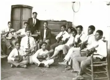 Fotografía antigua en blanco y negro de un grupo de personas reunidas frente a un edificio, posiblemente una escuela.