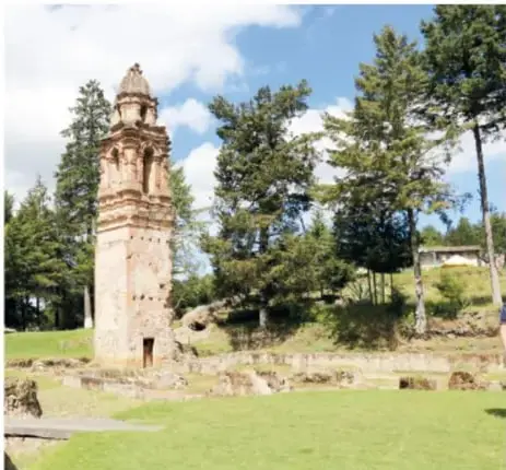 Fotografía de la torre de piedra en ruinas de una iglesia emergiendo entre árboles y césped, restos de un templo que quedó fuera del agua por la sequía.