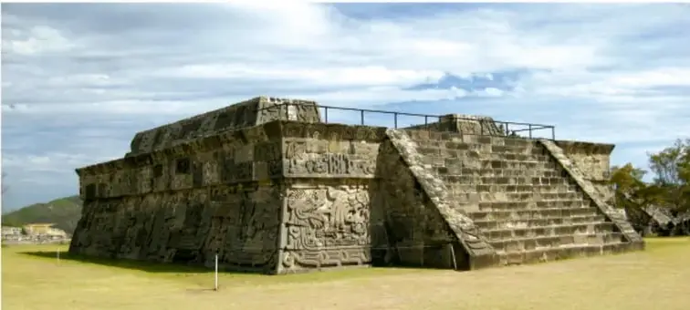 Fotografía de una pirámide o plataforma prehispánica de piedra con escalinatas, rodeada de césped, ilustrando las culturas antiguas de Mesoamérica.