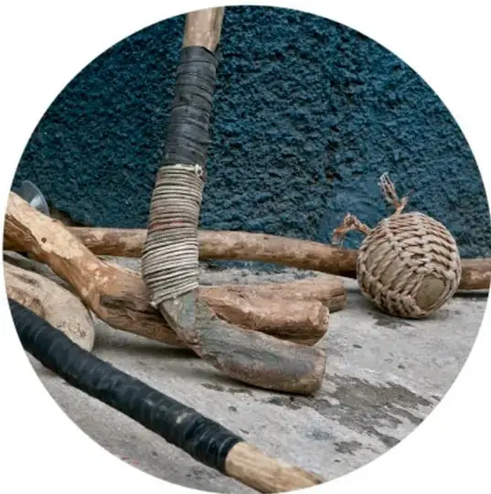 Fotografía de bastones de madera y una pelota tejida de fibra natural sobre una superficie oscura.