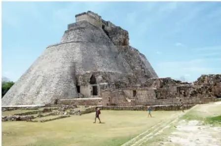 Edificio de varios cuerpos con esquinas redondeadas y patio con personas; es la Pirámide del Adivino, Uxmal.