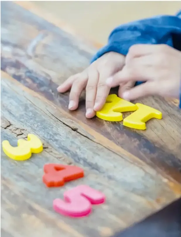 Niña acomodando dígitos de plástico de colores (3, 4, 5 y 1) sobre una mesa de madera.