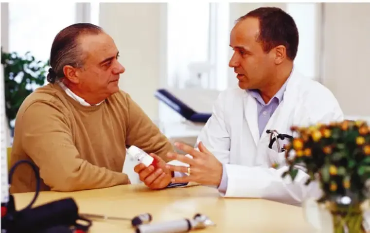 Fotografía de un médico de bata blanca con estetoscopio conversando con un paciente adulto mayor en un consultorio; transmite la importancia de la consulta médica y la orientación sobre salud sexual.