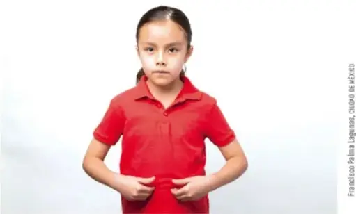 Fotografía de una niña con playera roja que sostiene sus manos juntas a la altura del pecho, como si estuviera exponiendo.