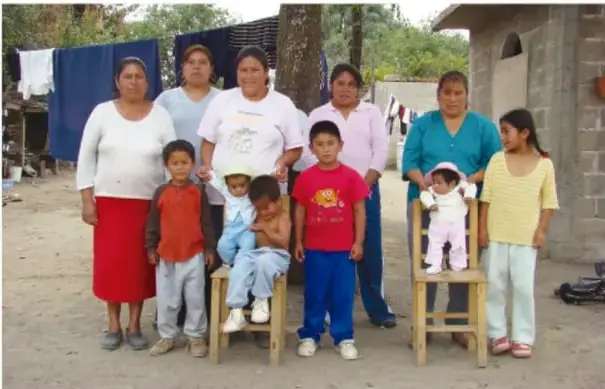 Grupo de mujeres, ninos y ninas de una comunidad posando al aire libre frente a una casa.