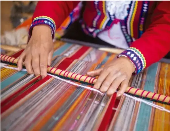 Fotografía de manos tejendo en un telar tradicional con hilos de colores, ilustrando un proceso técnico de uso sustentable.