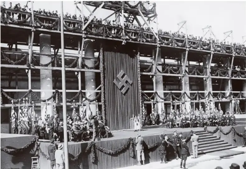 Fotografía en blanco y negro de un gran acto político nazi en un estadio, con banderas con la esvástica y una multitud uniformada.