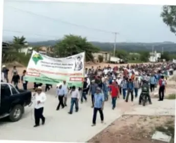 Fotografía de una marcha multitudinaria por una carretera, con pancartas y personas caminando entre vehículos.
