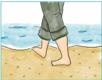 Piernas de un niño caminando descalzo sobre la arena de la playa.
