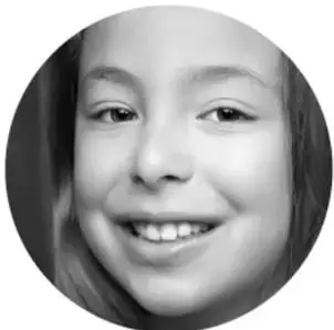 Fotografía circular en blanco y negro de una niña sonriente con dientes visibles, mirando a la cámara.