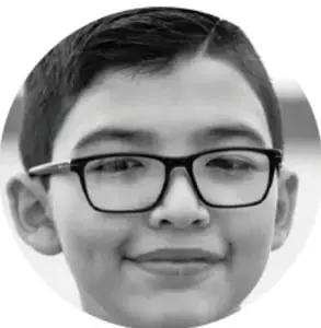 Fotografía de un niño con lentes y suéter, mirando a la cámara.
