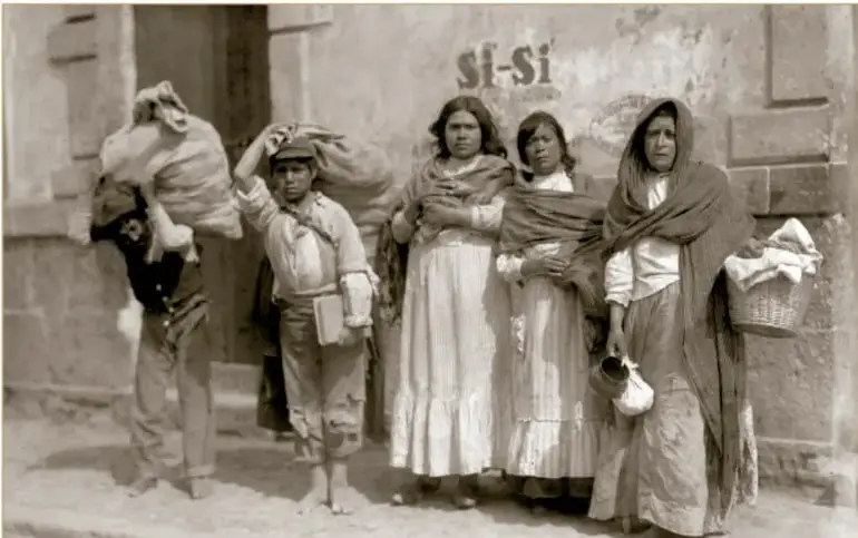 Fotografía histórica en sepia: mujeres y niños de origen humilde cargando bultos, canastas y pertenencias en una calle durante el armisticio de la Decena Trágica, 1913. Crédito: Secretaría de Cultura, INAH, SINAFO, FN.MX.