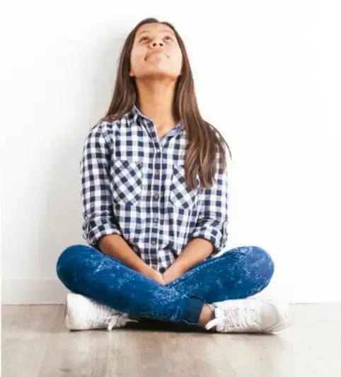 Fotografía de una adolescente sentada en el piso con las piernas cruzadas, ojos cerrados y rostro sereno, con la cabeza ligeramente inclinada hacia arriba; representa la reflexión y la introspección propias del autoconocimiento.