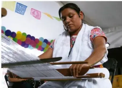 Fotografía de una mujer tejiendo en un telar tradicional, ilustrando el uso de herramientas e instrumentos en actividades artesanales.