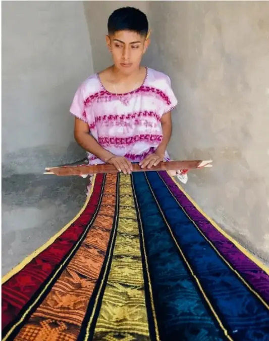 Detalle de telas tejidas de colores vivos con motivos geométricos colgadas en un telar.